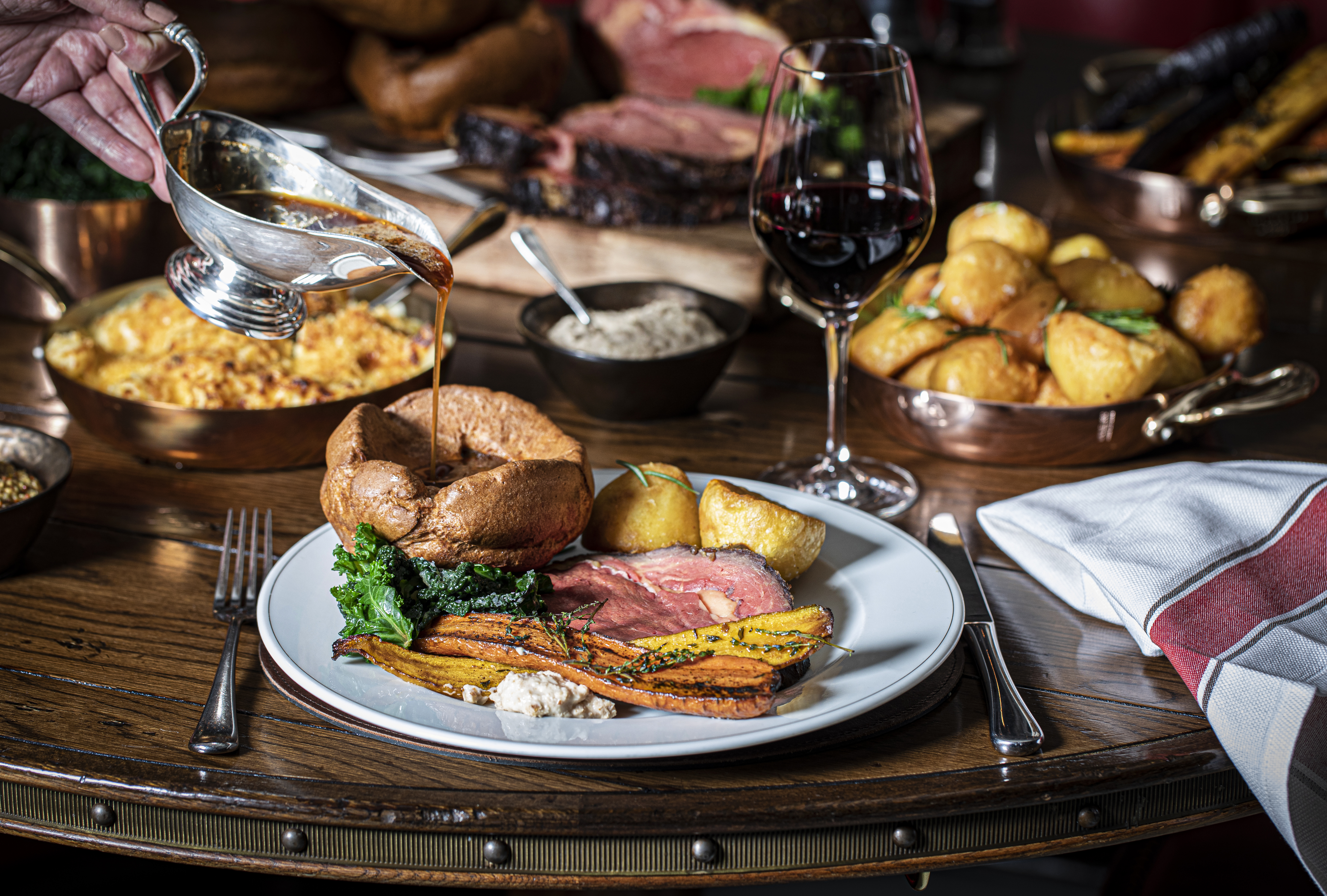 Traditional Sunday roast with gravy, vegetables, and red wine glass.