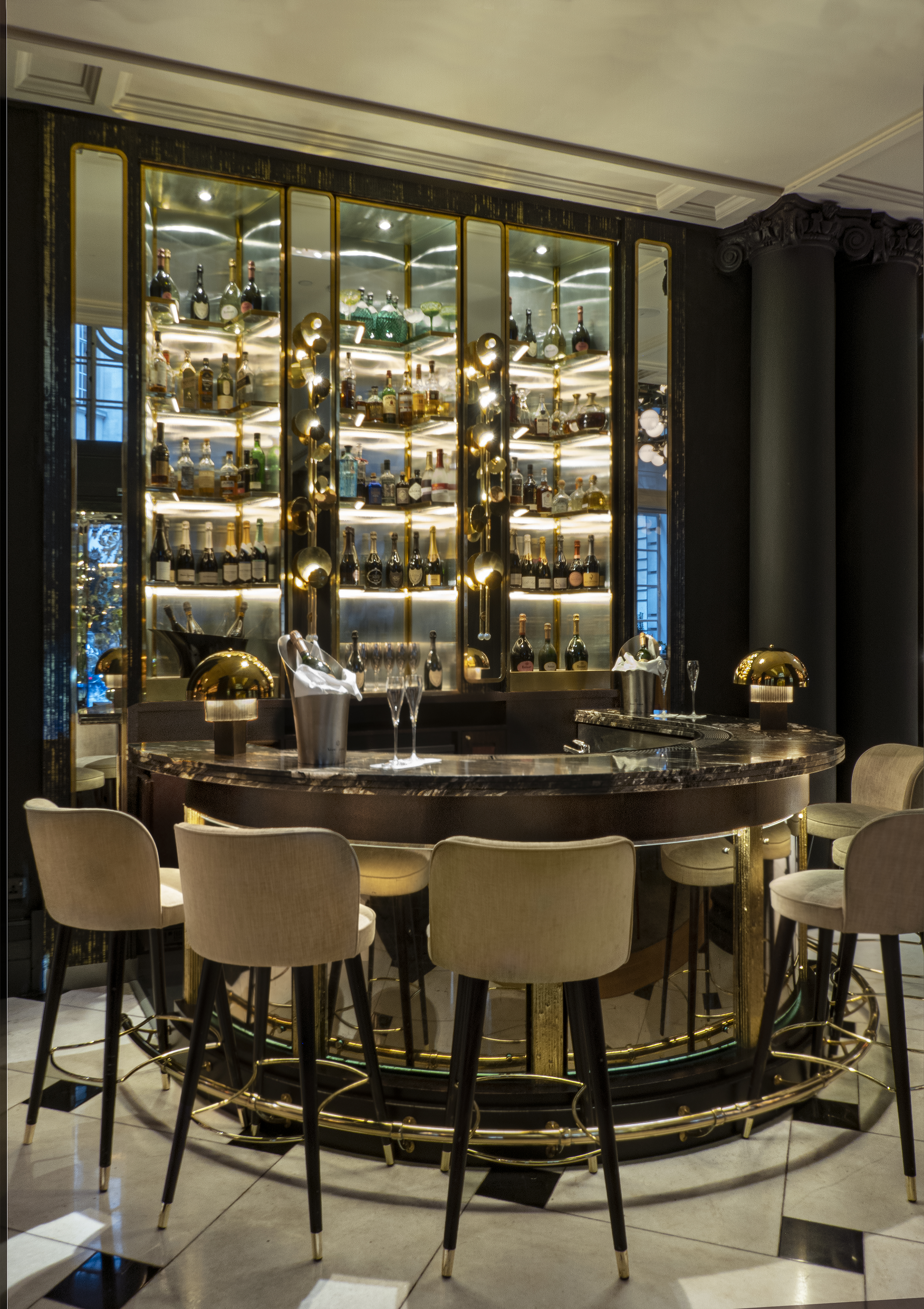 Luxurious hotel bar with marble counter, champagne glasses, and backlit liquor shelves.