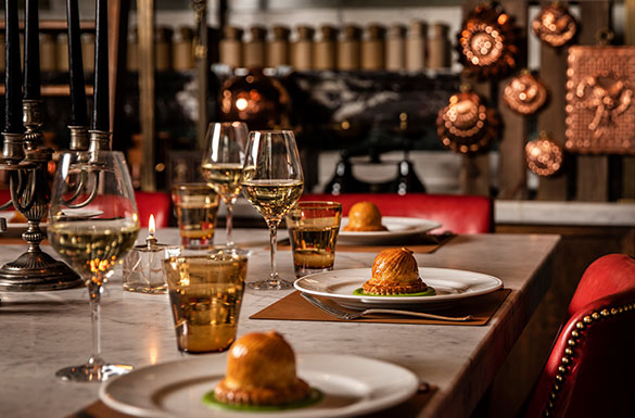 Elegant dining setup with gourmet pies, wine glasses, candles, and warm lighting.