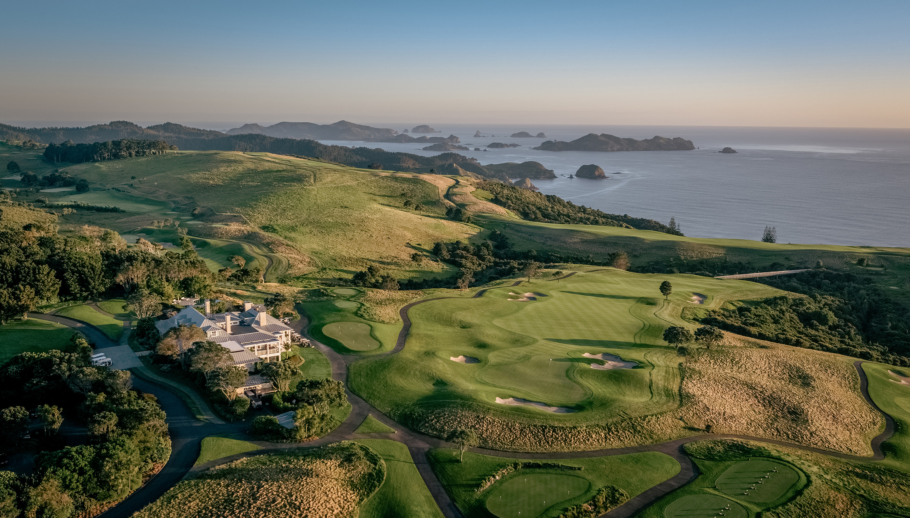 Aerial view of a coastal golf course surrounded by rolling hills and islands.