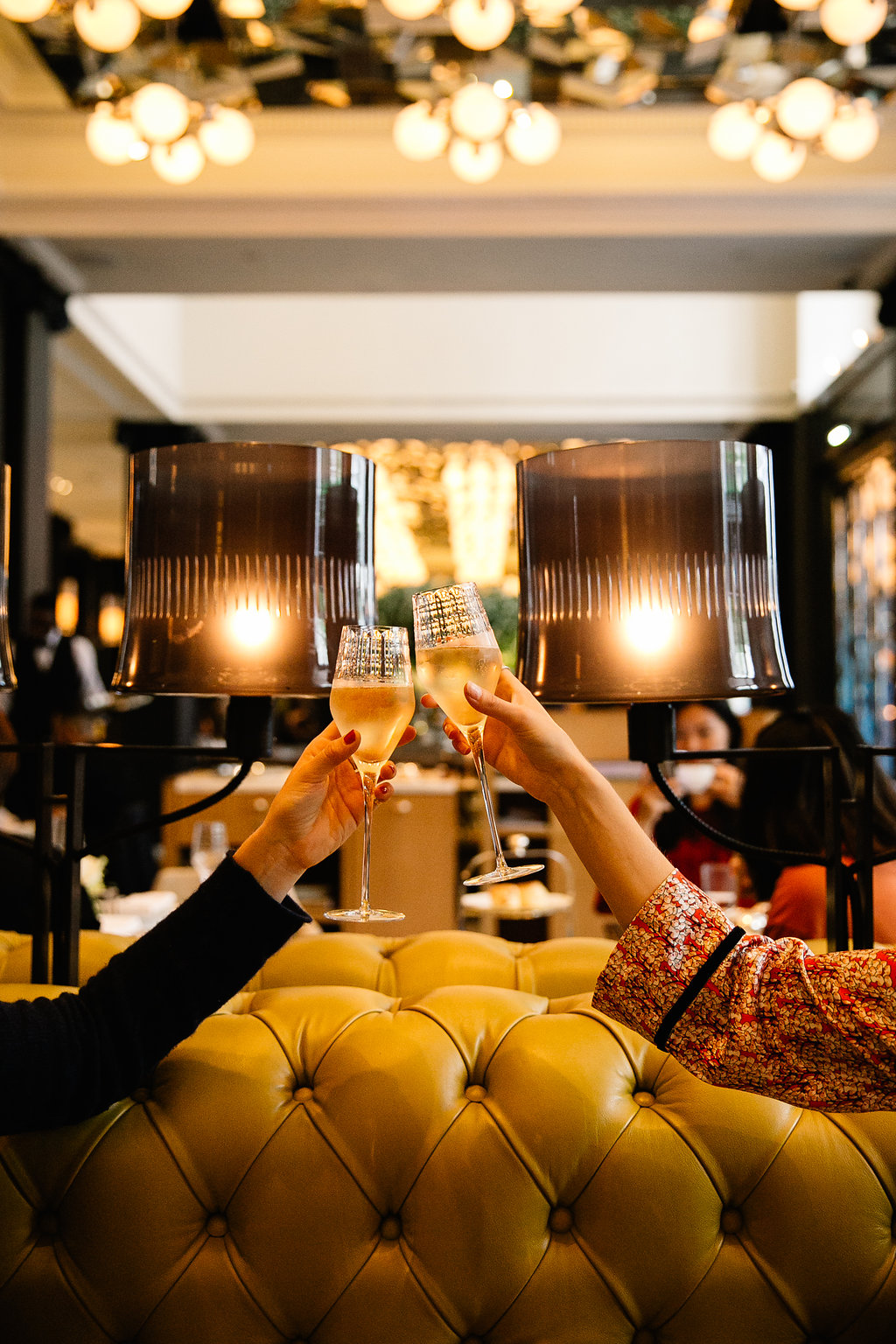 Two people clinking champagne glasses inside a stylish, warmly lit restaurant.